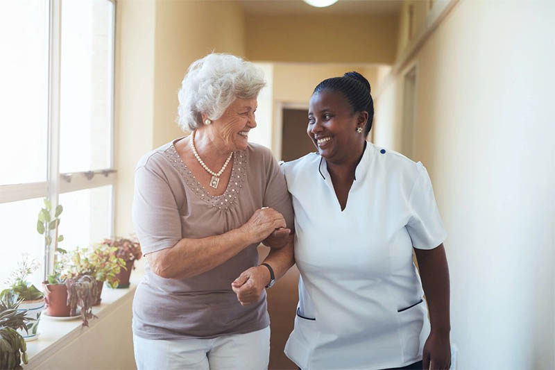 Elderly woman walking with a caregiver, smiling.