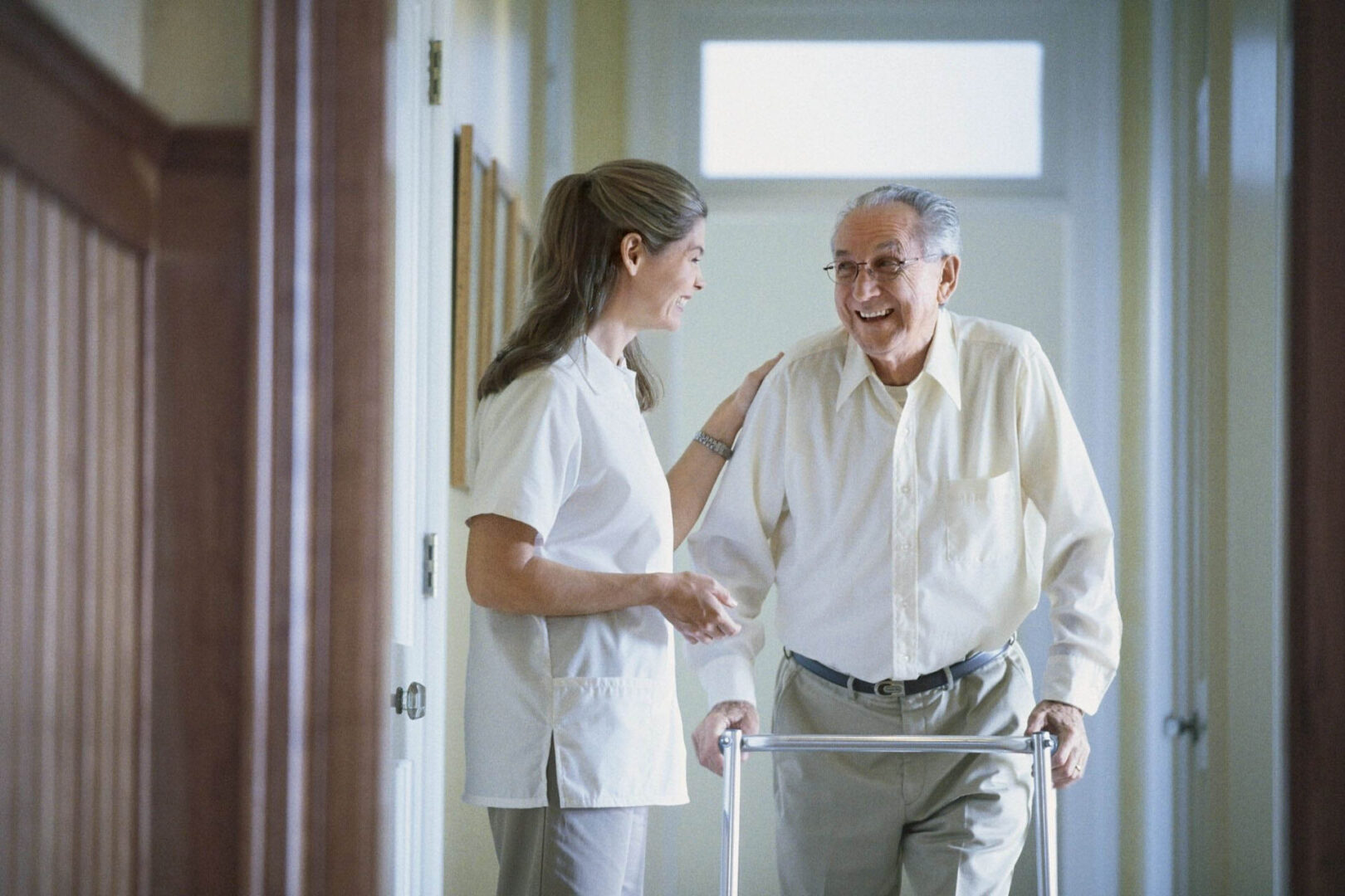 Elderly man with walker and caregiver smiling.