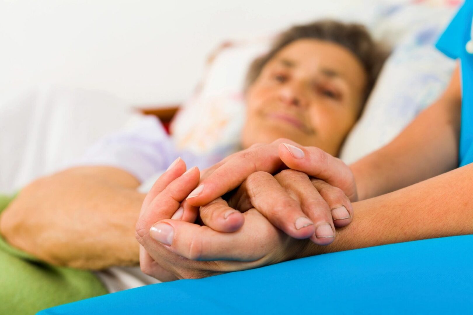 Caregiver holding elderly woman's hands in bed