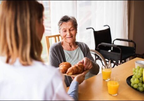 Elderly woman receiving breakfast from caregiver.