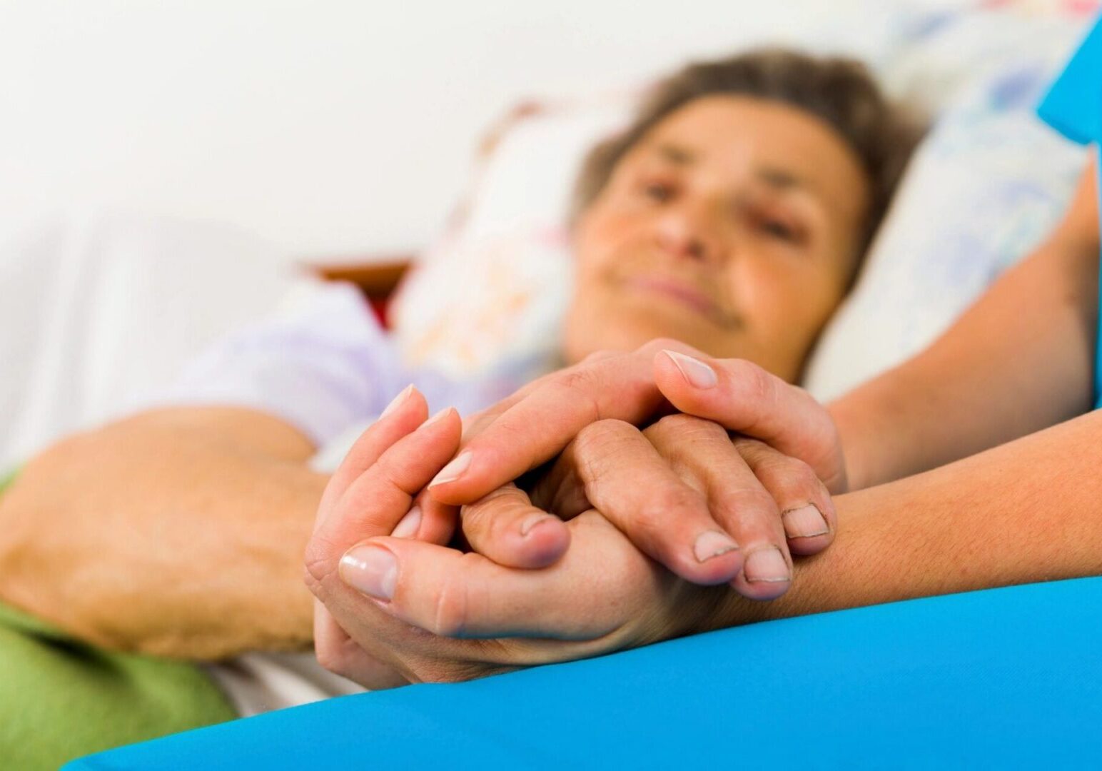 Caregiver holding elderly woman's hands in bed
