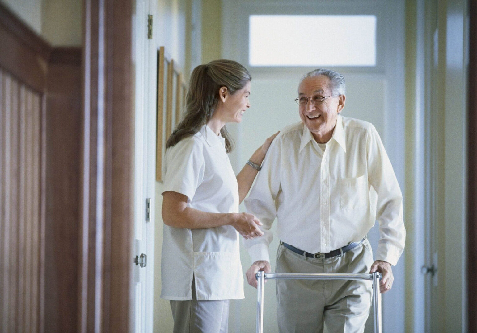 Elderly man with walker and caregiver smiling.